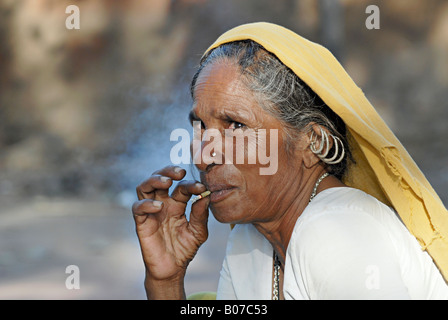 Vieille femme tribale fumant du bidi, une cigarette artisanale indienne faite de tabac ou de feuilles de beedi. Bhil tribu des visages ruraux de l'Inde Banque D'Images