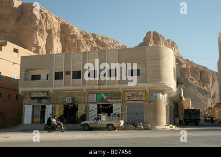 Homme avec une femme voilée sur une moto passer d'un bâtiment moderne, à Al Hawta dans la région du Yémen Hadhramawt Banque D'Images