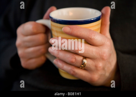 Femme d'âge moyen, berçant les mains une tasse de thé Banque D'Images