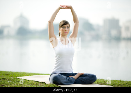 Une jeune femme est la pratique du yoga dans un parc près d'un lac. Banque D'Images