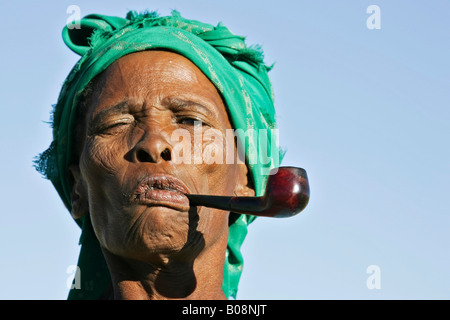 Vieille ridée face, femme namibienne desséché fumant une pipe et portant un green headwrap, Namibie, Afrique Banque D'Images
