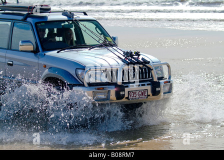 Toyota 4X4 SUV avec des cannes à pêche et de surf monté sur le capot et le toit de la conduite dans les projections d'eau sur la plage, Frase Banque D'Images