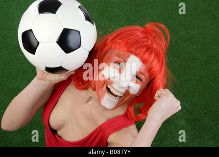 Cute woman in a Red top comme ventilateur Suisse, encourageant avec le football et le poing serré Banque D'Images