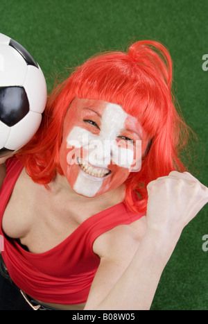 Cute woman in a Red top comme ventilateur Suisse, encourageant avec le football et le poing serré Banque D'Images