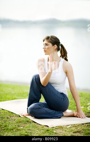 Une jeune femme est la pratique du yoga dans un parc près d'un lac. Banque D'Images