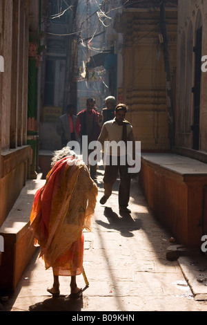 Une vieille femme dans un sari orange a du mal à faire son chemin une rue de la vieille ville de Varanasi, Inde Banque D'Images