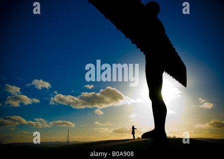 Silhouette de silhouette debout avec les bras étirés au pied de l'Ange du Nord à Gateshead. Vu contre un ciel bleu et jaune. Banque D'Images