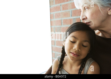 Senior woman posant son menton sur la tête de petite fille, les yeux fermés de la jeune fille Banque D'Images