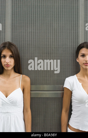 Teenage twin sisters debout devant la grille de métal, les deux looking at camera, portrait Banque D'Images