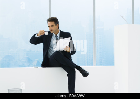 Portrait de la fenêtre à côté du lutrin, holding documents, boire du café Banque D'Images
