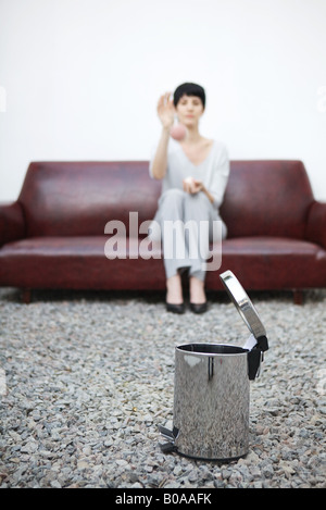 Femme assise sur le canapé, jetant à poubelle en premier plan Banque D'Images