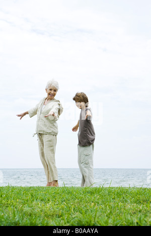 Grand-mère et petit-fils debout à l'extérieur avec les bras, ocean in background Banque D'Images