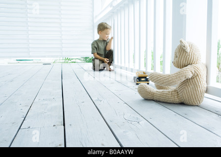 Petit garçon assis sur le porche près de l'ours en peluche et voiture jouet, à la balustrade par Banque D'Images