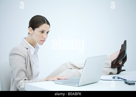 Businesswoman sitting at desk avec jambes, using laptop Banque D'Images