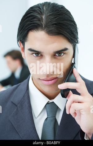 Young businessman using cellphone, smiling at camera, portrait Banque D'Images