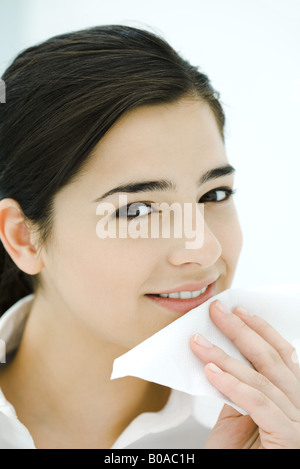 Young woman holding napkin contre bouche, smiling at camera Banque D'Images