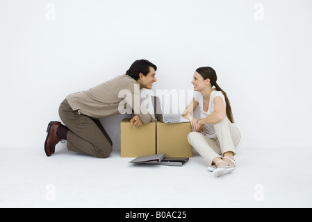 Couple sitting at desk with laptop computer de fortune entre eux, smiling at each other Banque D'Images