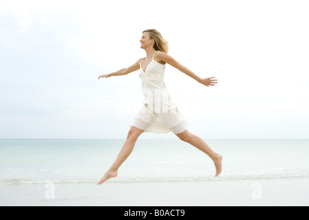 Femme sautant sur la plage, les bras, side view Banque D'Images