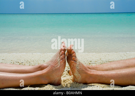 Deux ensembles de pieds et jambes couché sur la plage de sable tropicale de la mer bleu ciel bleu Banque D'Images