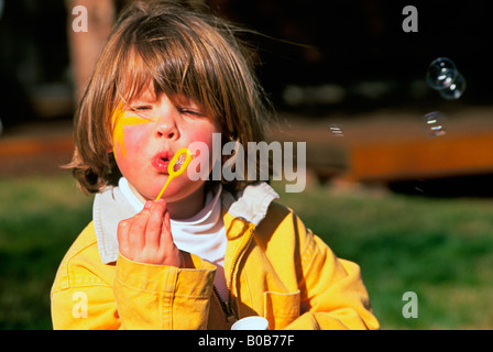 Une jeune fille souffle bulles avec un tuyau bulle dans sa cour avant Banque D'Images