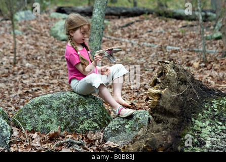 New York CAROLINE DU SUD Une belle jeune fille est assise sur un rocher couvert de mousse dans la forêt alors qu'elle enlève sa chaussure pour secouer les feuilles Banque D'Images