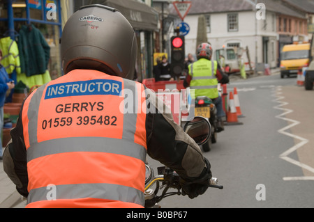 Instructeur moto donnant une leçon à rider - à la suite d'un élève conducteur alors qu'il s'arrête aux feux de circulation par les travaux routiers, Wales UK Banque D'Images