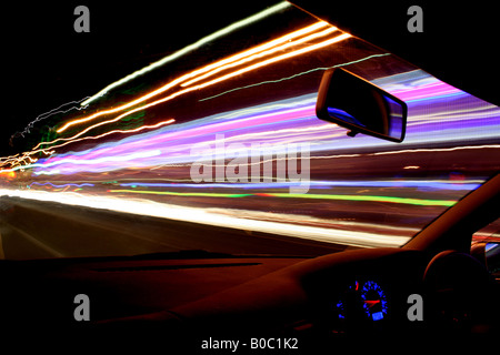 L'éclairage de rue, le trafic et la boutique-fronts produire de superbes sentiers de lumière que l'appareil photo par traînées dans une voiture en mouvement rapide Banque D'Images