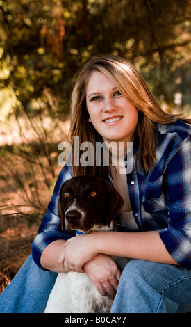 Image d'une adolescente blonde habillée d'une chemise de flanelle blanc bleu jeans et assis avec ses bras autour d'un chien d'oiseaux de chasse Banque D'Images