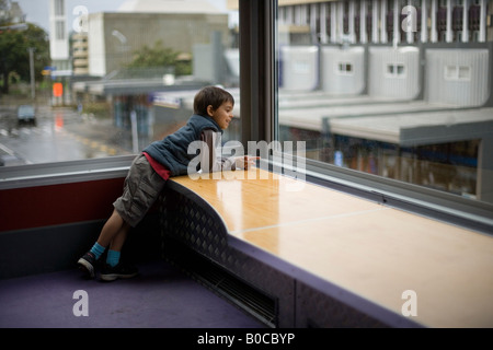 Garçon de 6 ans regarde par la fenêtre de la bibliothèque, Palmerston North, Nouvelle-Zélande Banque D'Images