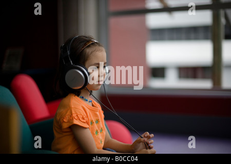 Bibliothèque centrale Palmerston North Nouvelle Zélande quatre ans, fille, à l'écoute des émissions de radio à l'aide d'écouteurs Banque D'Images