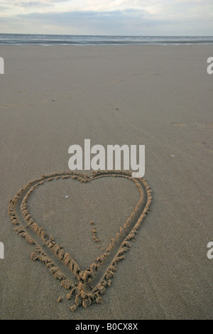Un amour coeur dessiné dans le sable sur une plage au coucher du soleil Banque D'Images