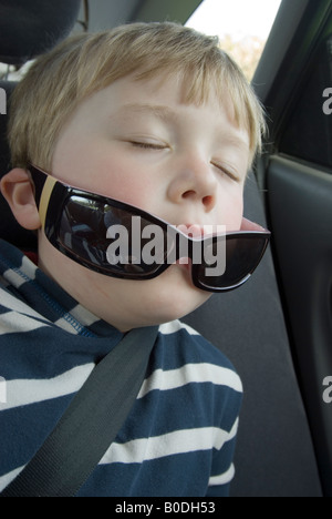 Jeune garçon endormi dans la voiture portant des lunettes de soleil Banque D'Images