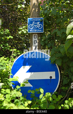 Bleu et blanc britannique de signalisation, tourner à gauche et un itinéraire cycliste partiellement masqué par la végétation Banque D'Images