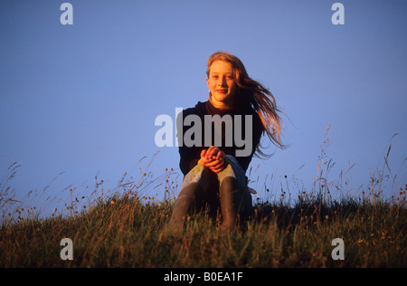 Jeune adolescente assis sur une colline baignée de lumière et de vent coucher du soleil d'or dans ses cheveux Hambledon Hill Dorset Banque D'Images