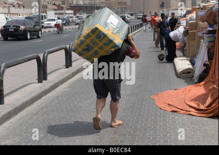 Dubaï, Émirats arabes unis (EAU). Un porteur porte une lourde charge sur ses épaules le long des quais de la vieille ville Banque D'Images