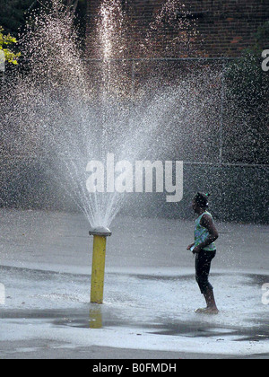 Un African American girl joue par une fontaine d'eau dans les petites rues de la ville de New York. Photo de Tom Zuback Banque D'Images