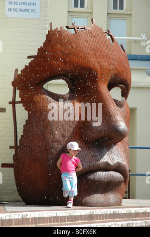 Petite fille devant le théâtre Marlowe avec sculpture à visage géant le Friars Canterbury Kent Banque D'Images