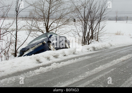 Une voiture épave se trouve dans un fossé sur une route de campagne après une forte tempête de neige. Banque D'Images