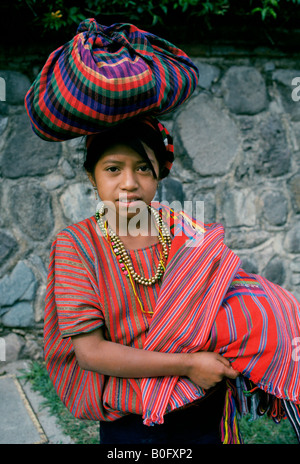 Une jeune fille habillée de façon traditionnelle avec son marché promenades pour commercialiser des biens sur sa tête à Antigua, Guatemala. Banque D'Images