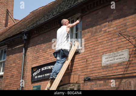 Staffordshire UK Homme Mai window cleaner en équilibre sur une échelle, le nettoyage des vitres avant de bâtiment historique Banque D'Images