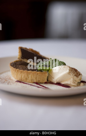 Riche d'une tarte au chocolat servi avec de la crème caillée, menthe fraîche et un filet de la sauce aux cerises Banque D'Images