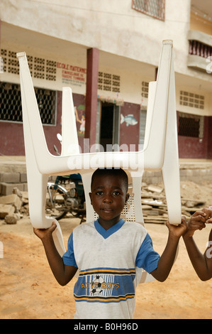 Jeune garçon portant une chaise en plastique sur sa tête, Douala, Cameroun, Afrique Banque D'Images