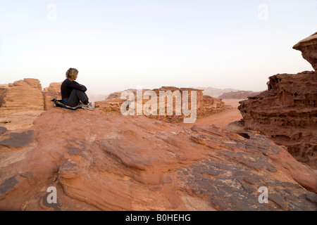 Femme assise sur une saillie rocheuse à la recherche au loin dans la distance, Wadi Rum, Jordanie, Moyen-Orient Banque D'Images