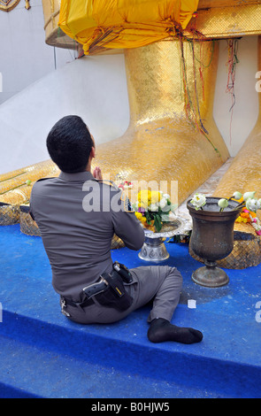 Agent de police en uniforme, priant au pied d'une gigantesque statue en or, temple Wat Intrawihan, Bangkok, Thaïlande, Asie du Sud-Est Banque D'Images