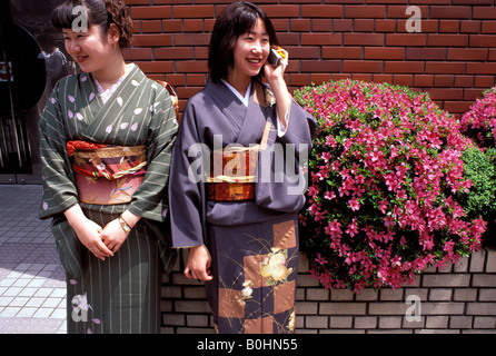 Les jeunes femmes vêtues de kimonos, l'un à l'aide d'un téléphone mobile, le Japon. Banque D'Images