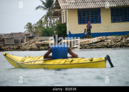 Un kayakiste de mer pagaies passé un Yula Kuna village sur l'île de isla tigre dans les îles San Blas, Panama Banque D'Images