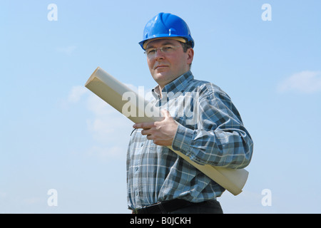 Site de construction manager wearing blue helmet holding rouleau de plans de bâtiment plus de ciel bleu Banque D'Images
