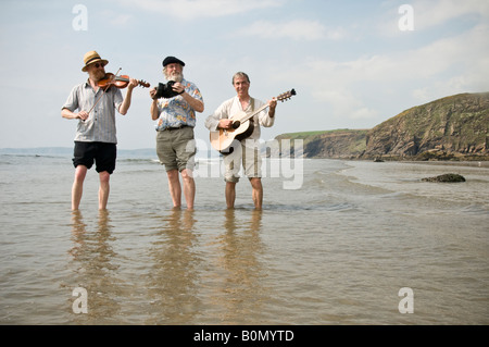 Trois musiciens folk acoustique traditionnelle jouant de la musique sur la plage et mer à pagayer dans le Pembrokeshire Druidston Haven UK Banque D'Images