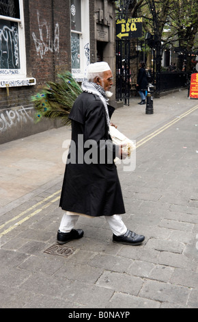 Bangladais âgés man crossing Brick Lane avec plumes de paon à vendre Banque D'Images