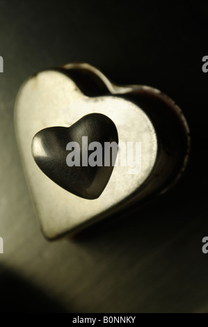 Petit coeur en acier avec de plus gros gâteau en forme d'acier non mise au point derrière Banque D'Images